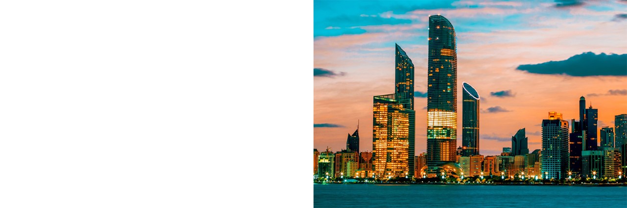 Das Bild zeigt die Skyline von Abu Dhabi bei Sonnenuntergang. Die beleuchteten Wolkenkratzer spiegeln sich im Wasser, während der Himmel in Orangetönen gefärbt ist.