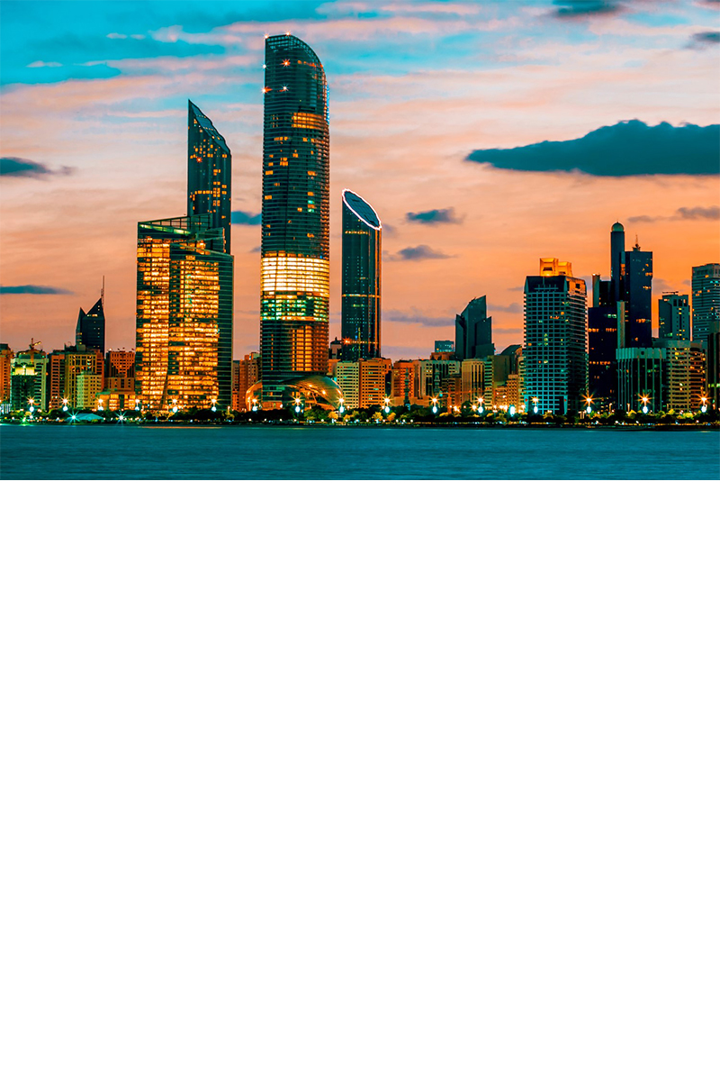 Das Bild zeigt die Skyline von Abu Dhabi bei Sonnenuntergang. Die beleuchteten Wolkenkratzer spiegeln sich im Wasser, während der Himmel in Orangetönen gefärbt ist. 