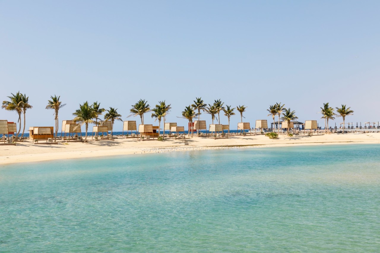 Blick vom klaren, blauen Wasser auf einen weißen Sandstrand mit Palmen und Strandkabinen.  © Fredy Thürig/stock.adobe.com 