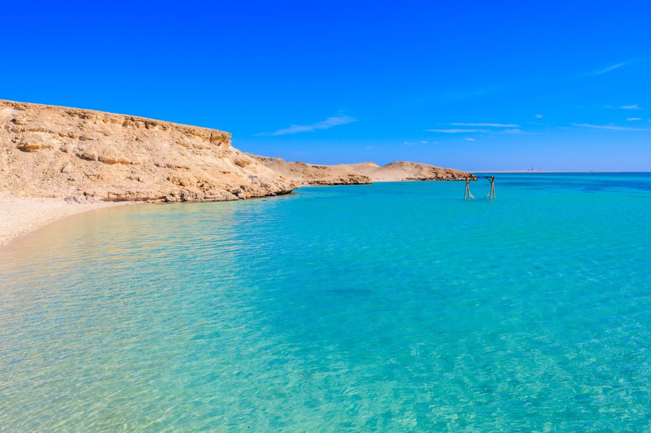 türkisblaues Wasser mit Sandstrand auf Giftun Island, felsige Küste im Hintergrund 