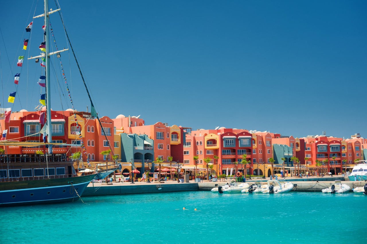 Strandpromenade Marina in Hurghada, bunte Häuserzeile hinter türkisblauem Wasser, Boote liegen im Hafen  