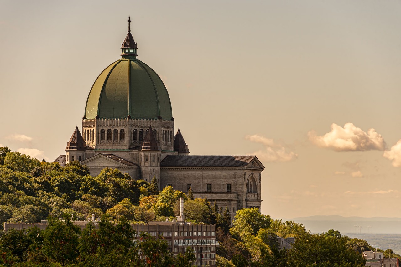 Großes, kuppelgekröntes Kirchengebäude, das auf einem Hang steht und in warmes, goldenes Licht getaucht ist; Treppen und Grünflächen führen hinauf.