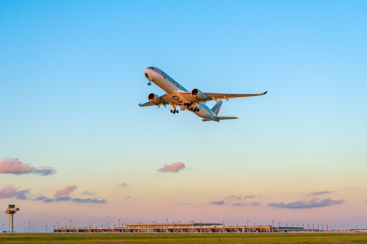 Maschine von Qatar Airways startet am BER. Dahinter das Terminal und der Tower im Abendlicht.