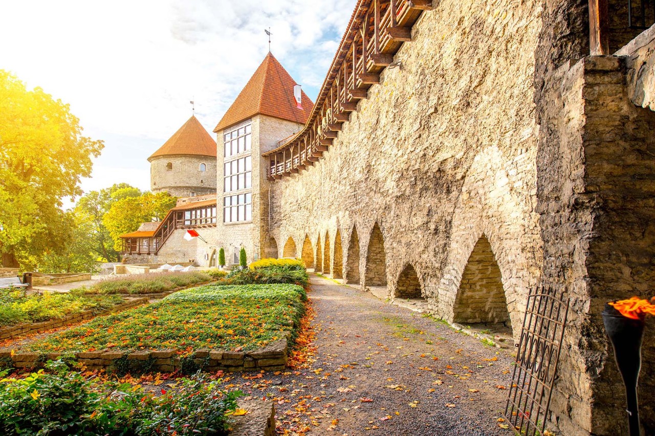 Alte Stadtmauer mit Rundturm und Ziegeldach bei Sonnenschein.