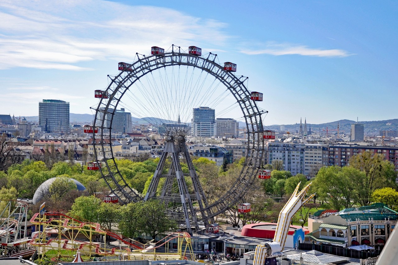 Riesenrad im Prater vor moderner Stadtlandschaft.