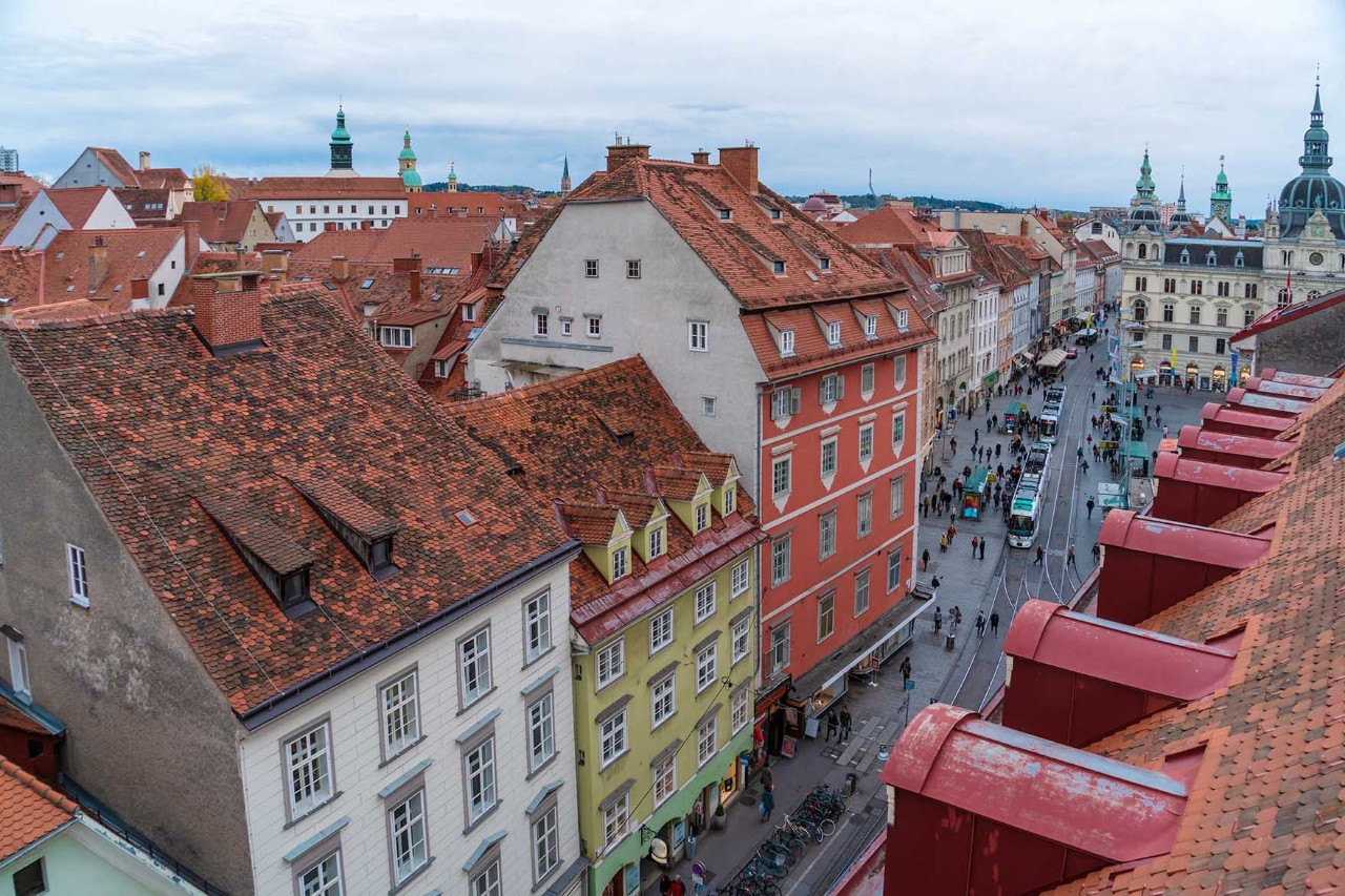 Flaniermeile in Graz mit Straßencafés, Passanten und historischen Gebäuden.