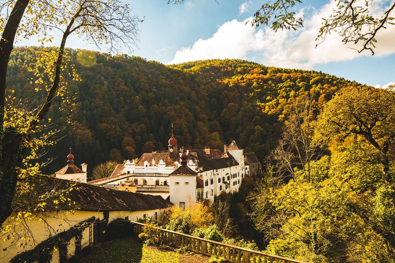 Schloss Herberstein mit Zinnen, Türmen und Gartenanlage in grüner Hügellandschaft.