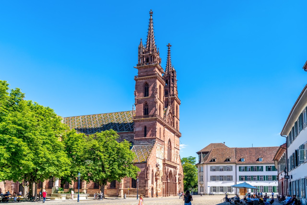 Ruhiger Platz in Basel mit roter Kirche, alten Domherrenhäusern, Bäumen und einem Café 
