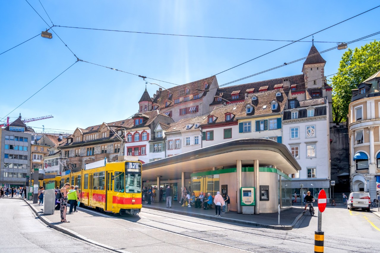 Barfüsserplatz mit Menschen, Straßenbahn und Häusern an einem sonnigen Tag 