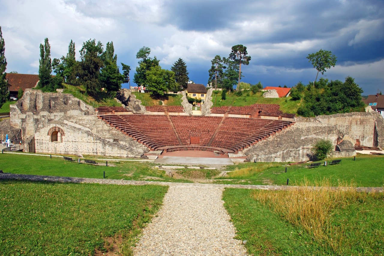 Das halbrunde Amphitheater als Teil eines Freilichtmuseums inmitten grüner Wiesen und Bäume 