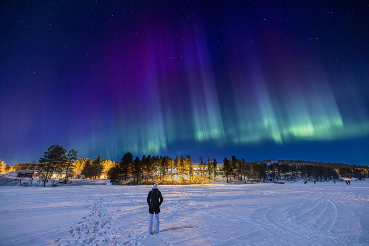 Polarlichter über Schneelandschaft mit allein stehender Person.