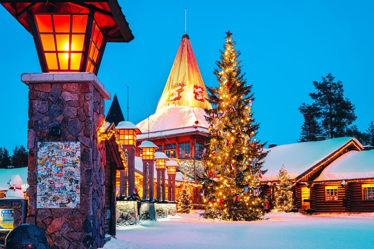 Weihnachtlich beleuchtetes Dorf mit Tannenbaum im Schnee.