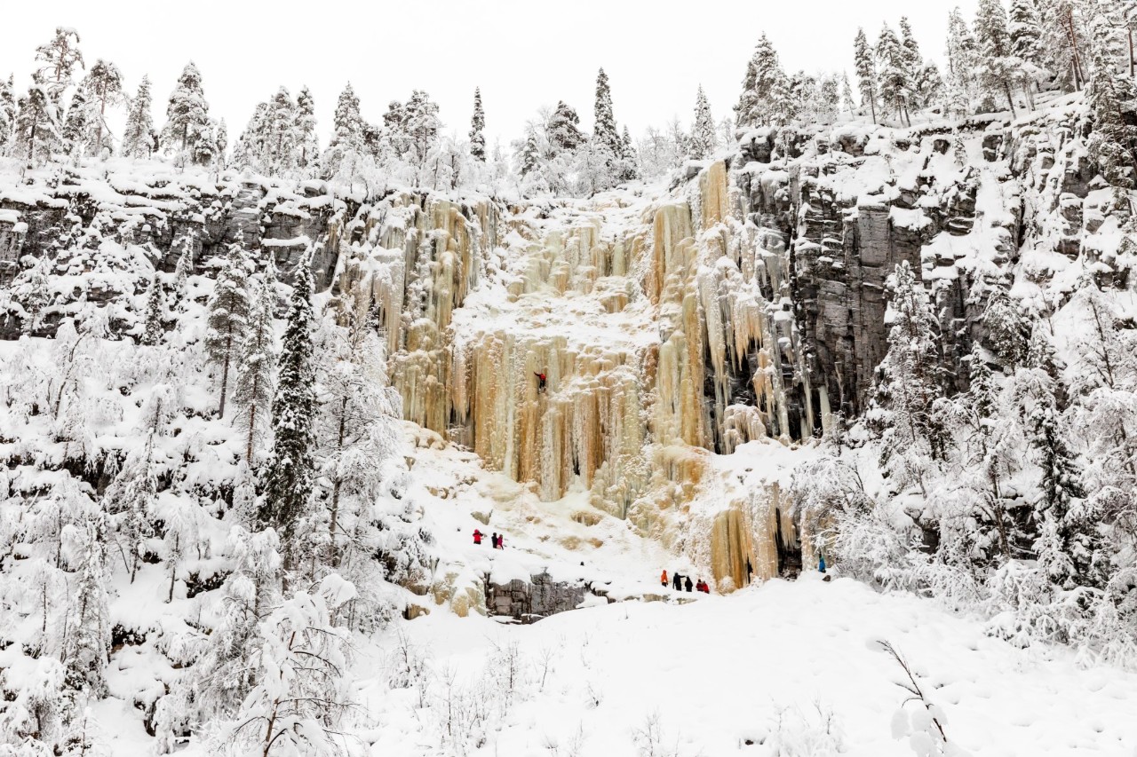 Gefrorener Wasserfall in verschneiter Felswand mit Kletterern.
