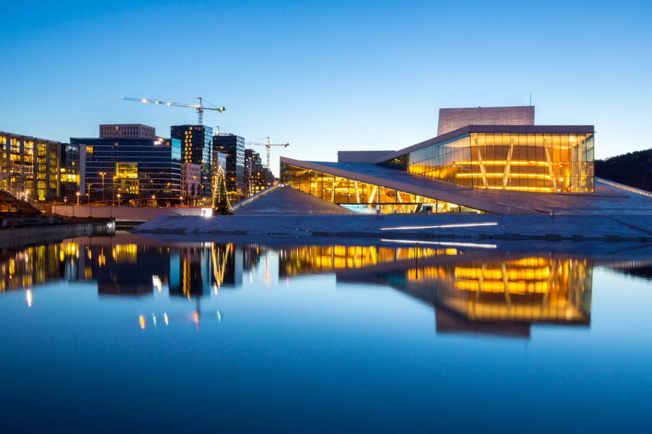 Beleuchtetes Opernhaus in Oslo am Abend mit Spiegelung im Wasser.