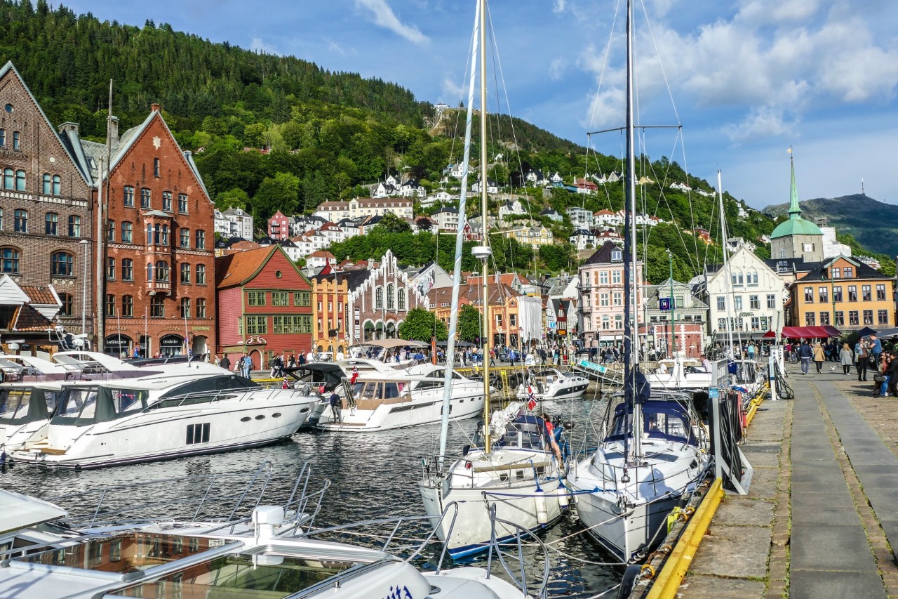 Boote im Hafen von Bergen mit umliegenden Häusern und Bergen im Hintergrund.