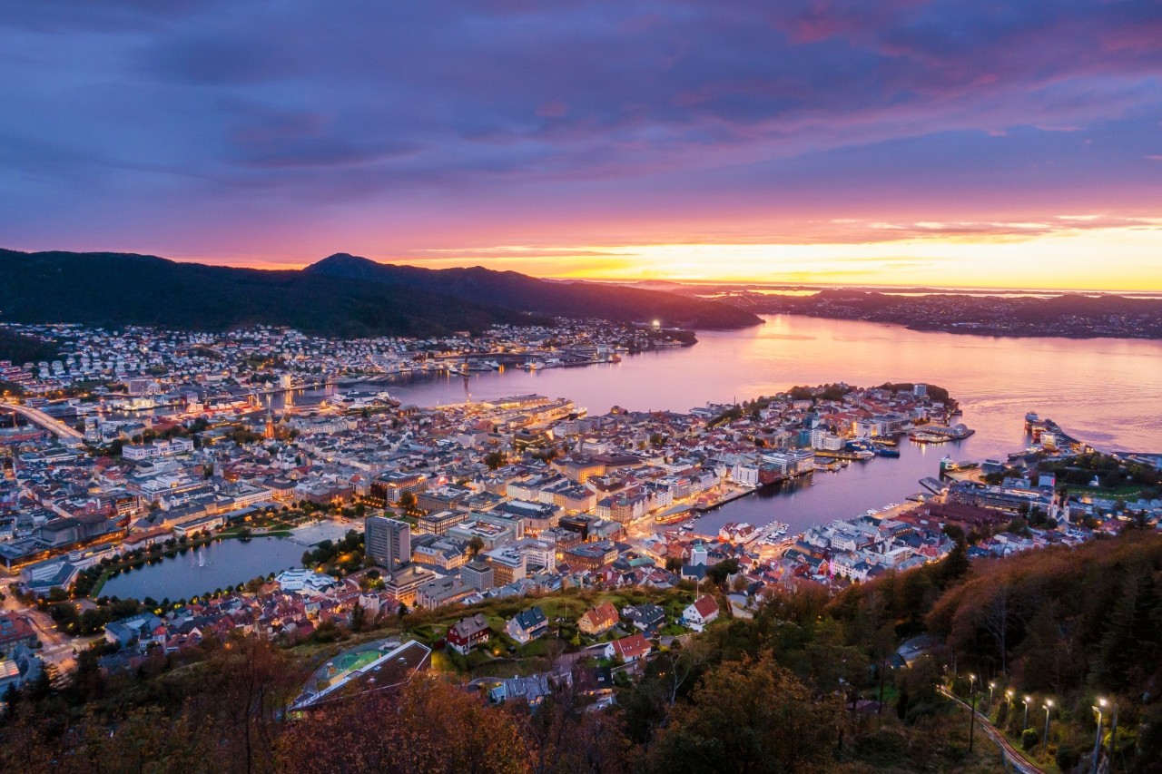 Bergen und Hafen im Abendlicht vom Berg Fløyen mit Lichtern der Stadt.