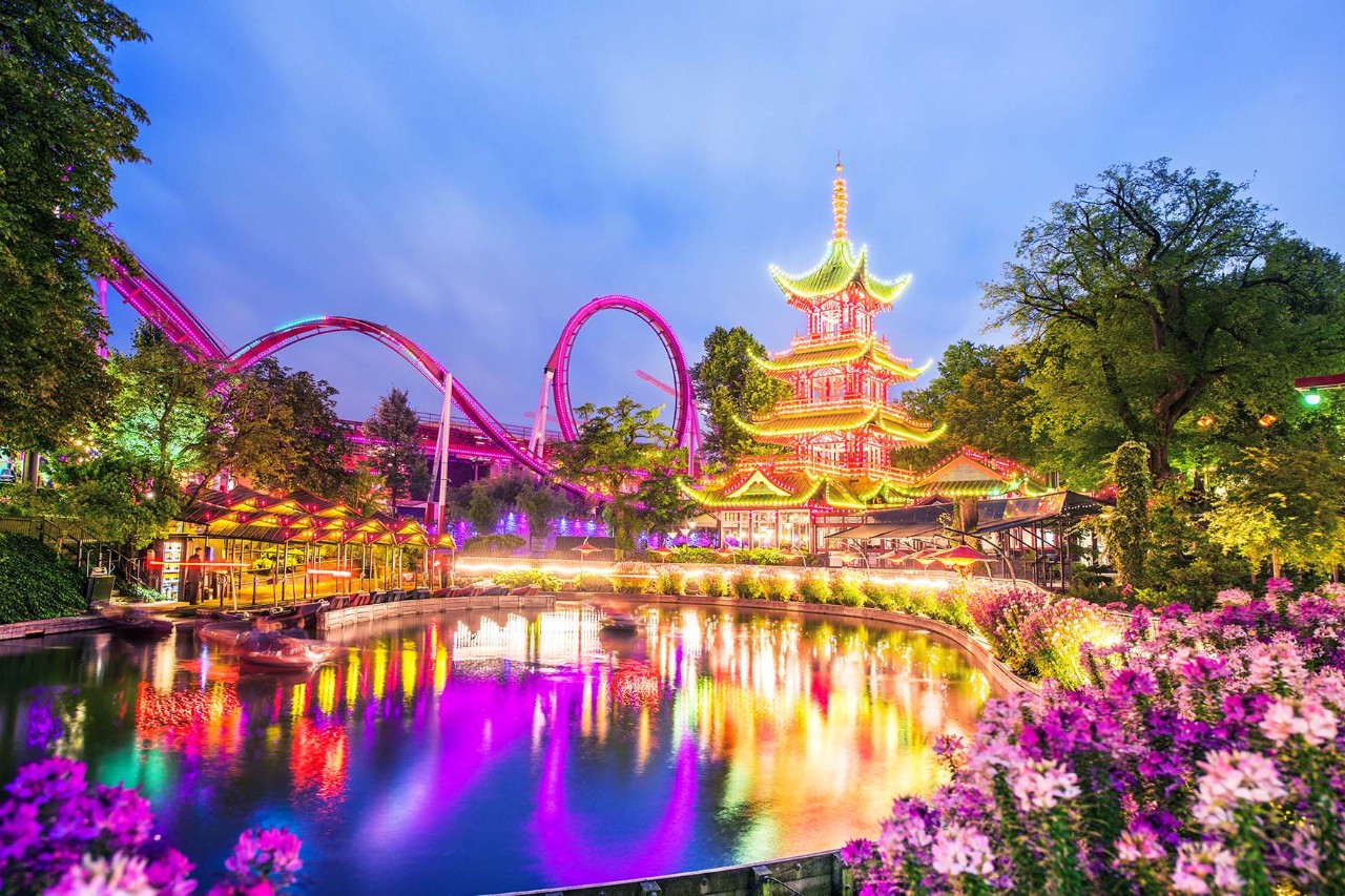 Abendstimmung im Tivoli mit beleuchteten Fahrgeschäften und bunten Lichtern.
