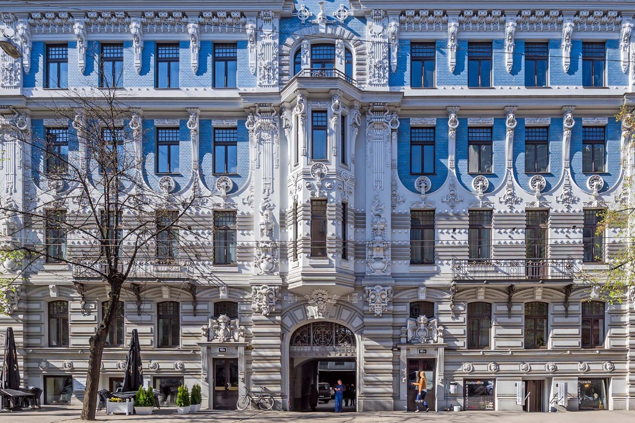 Jugendstilfassade mit verzierten Erkern und weiblicher Skulptur am Balkon.