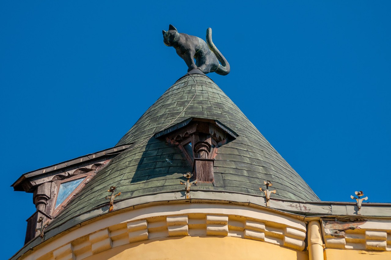 Das gelbe Katzenhaus  mit spitzem Turm und Katzenfigur auf dem Dach.