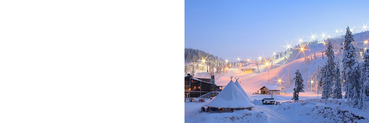 Winterliche Skilandschaft bei Dämmerung mit beleuchteten Pisten, verschneiten Bäumen, Hütten und einem kegelförmigen Zelt im Vordergrund. 