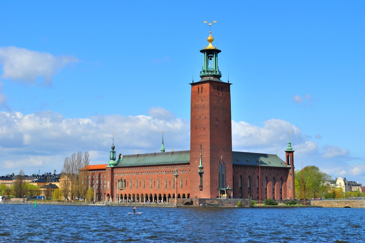 Stadshuset mit Turm und Segelbooten vor blauem Himmel.