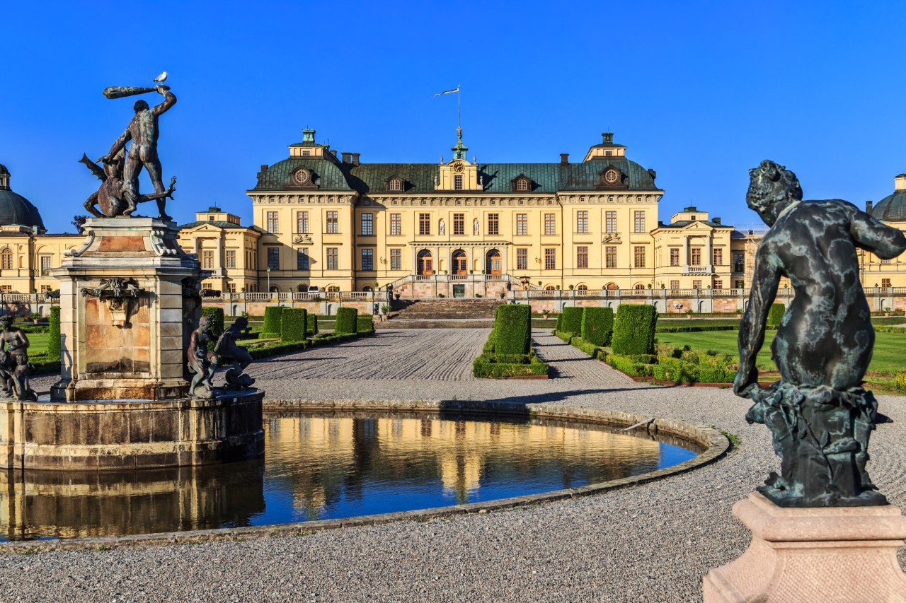 Brunnen mit Figuren vor dem Schloss Drottningholm und gepflegtem Garten.