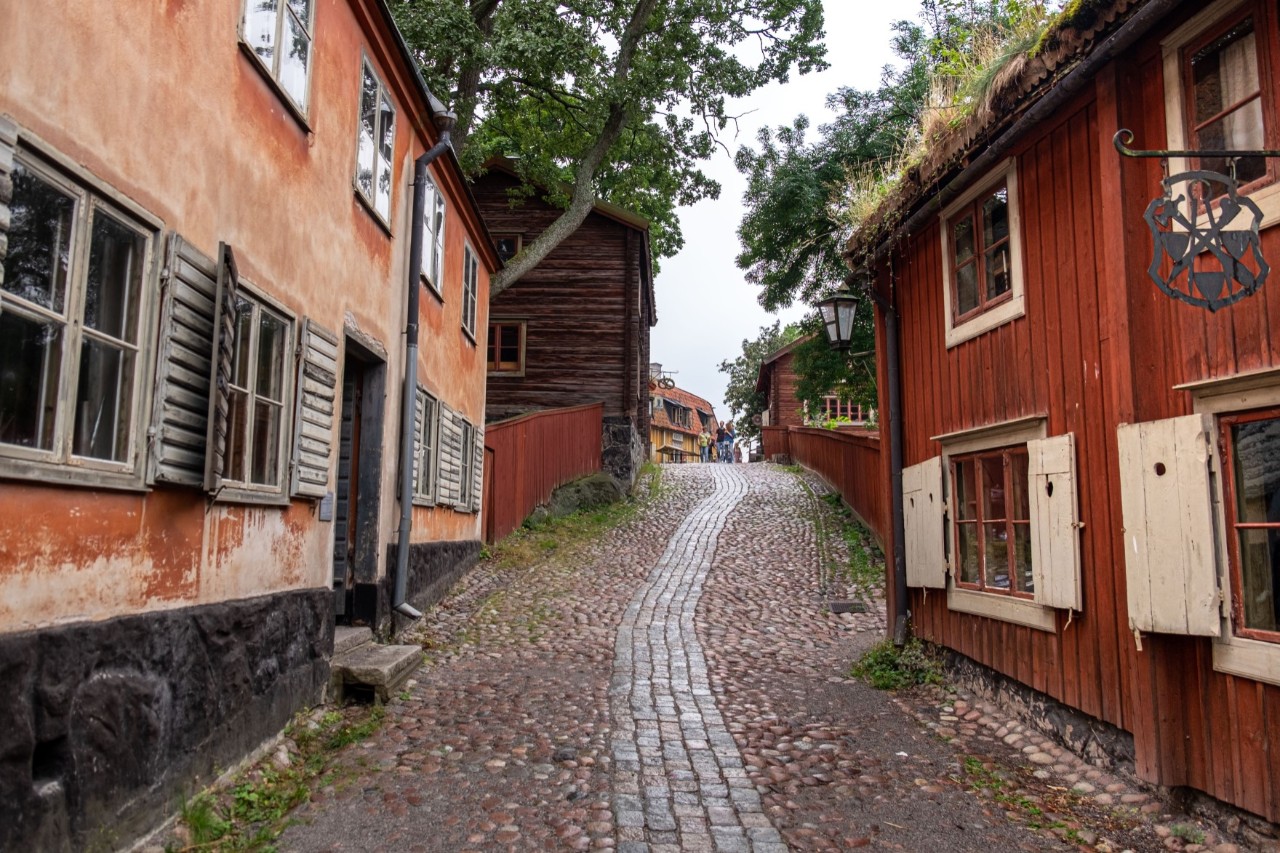 Skansen-Freilichtmuseum mit gepflastertem Weg und Holzhäusern.