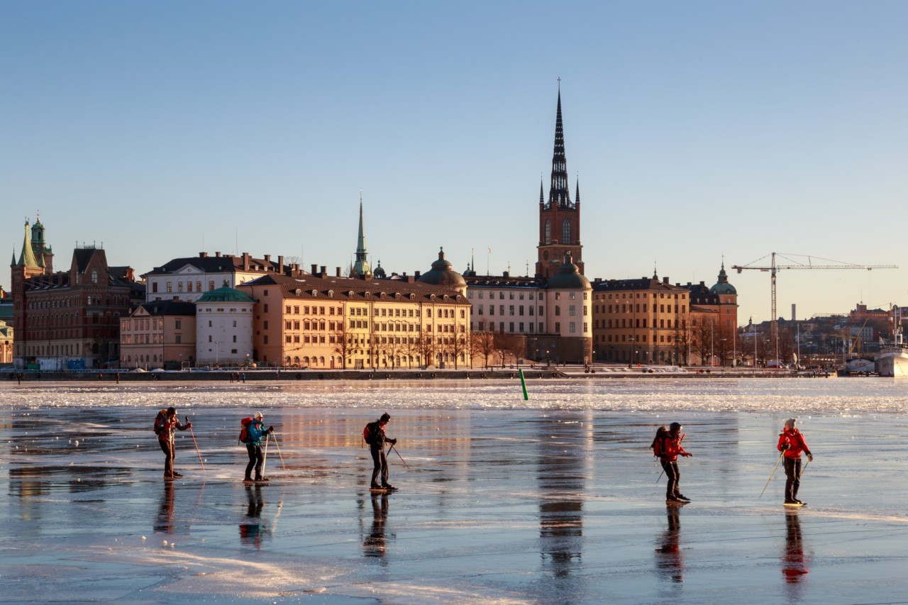 Menschen auf zugefrorenem See vor historischen Gebäuden in Stockholm.