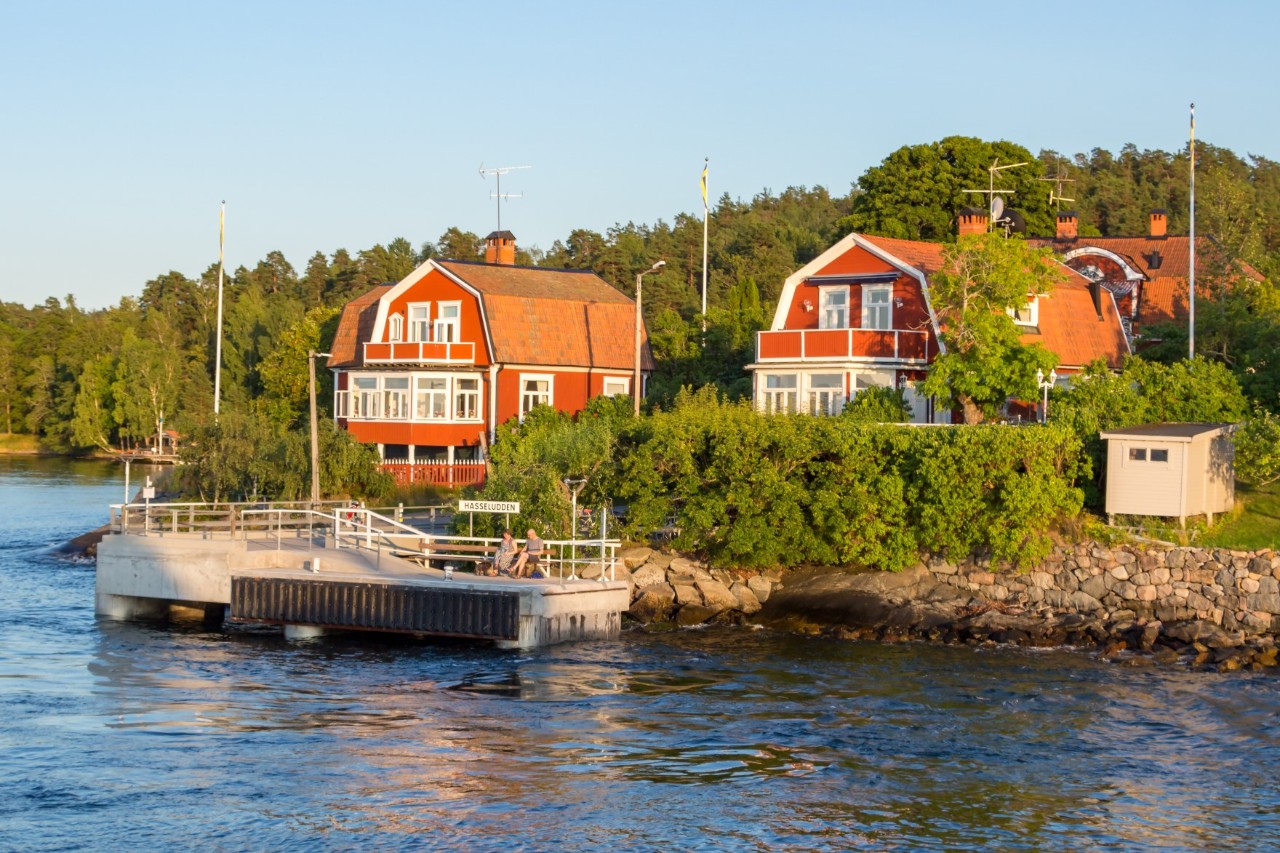 Rotes Bootshaus am Ufer mit weißem Ruderboot und Felsen.