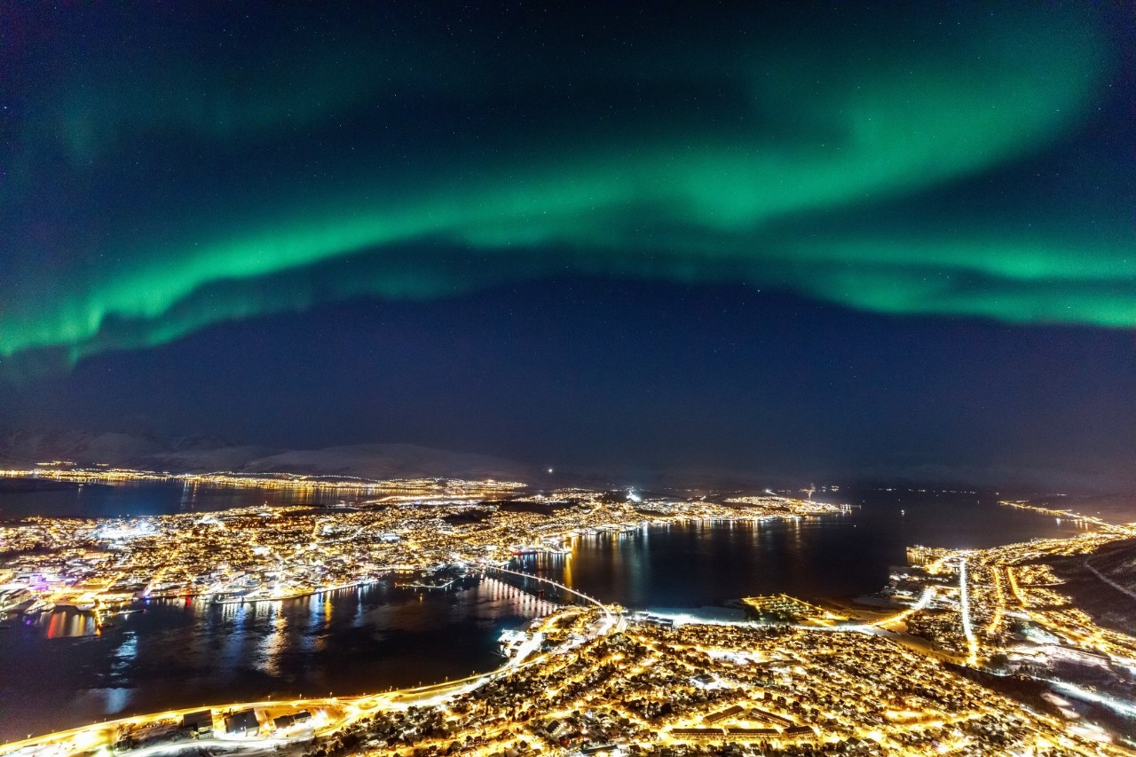 Nordlichter über Tromsø bei Nacht, mit Blick auf Stadtlichter und Wasser.