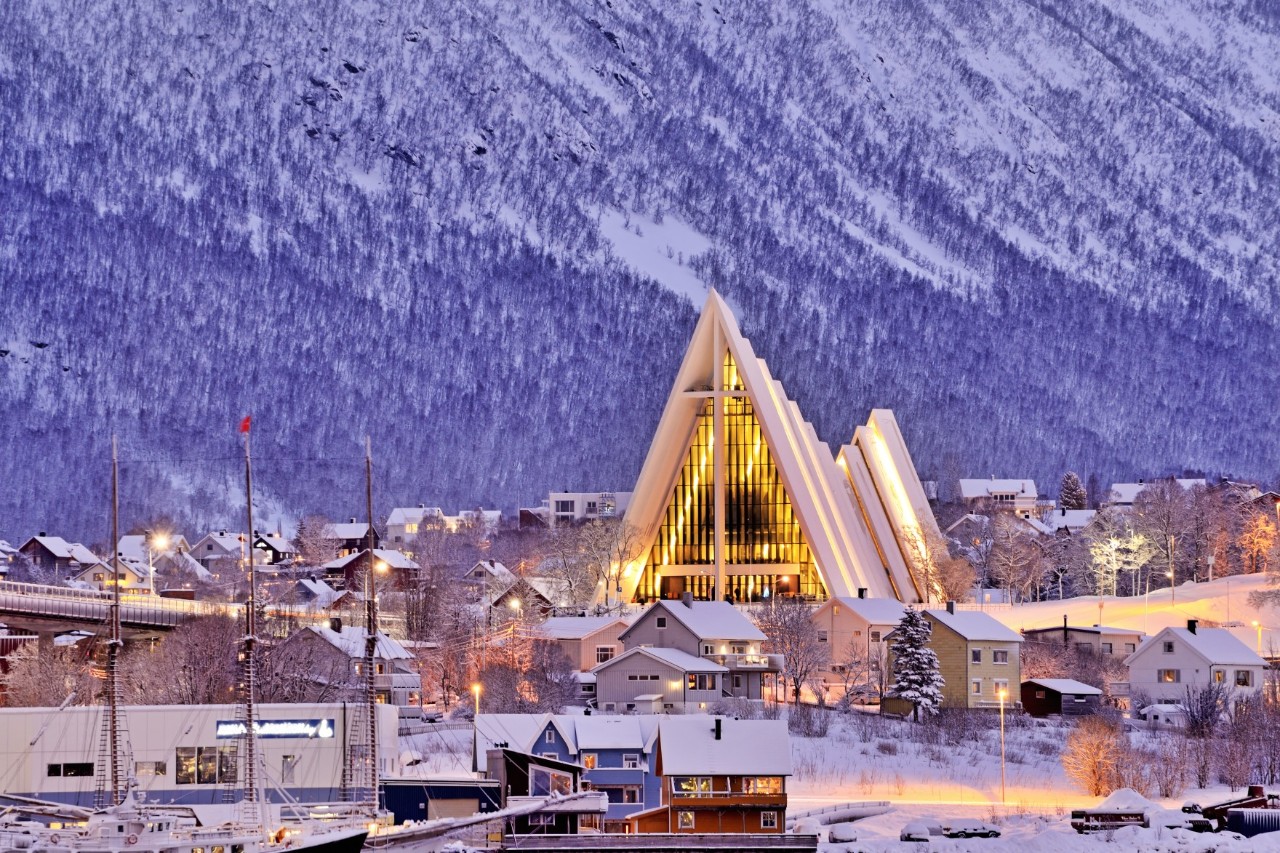 Beleuchtete Eismeerkathedrale vor verschneitem Bergpanorama in Tromsø.