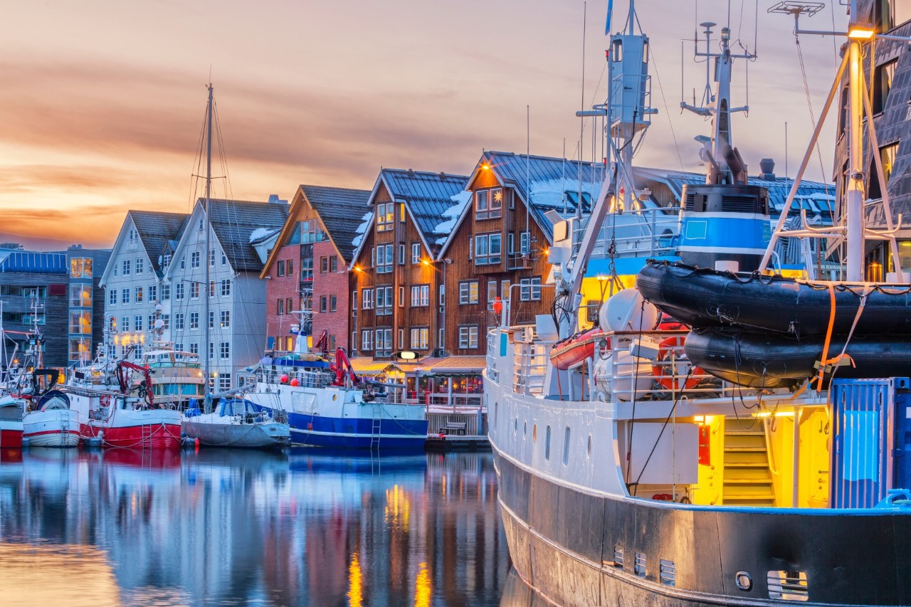 Fischerboote vor bunten Holzhäusern im Hafen von Tromsø bei Sonnenuntergang.