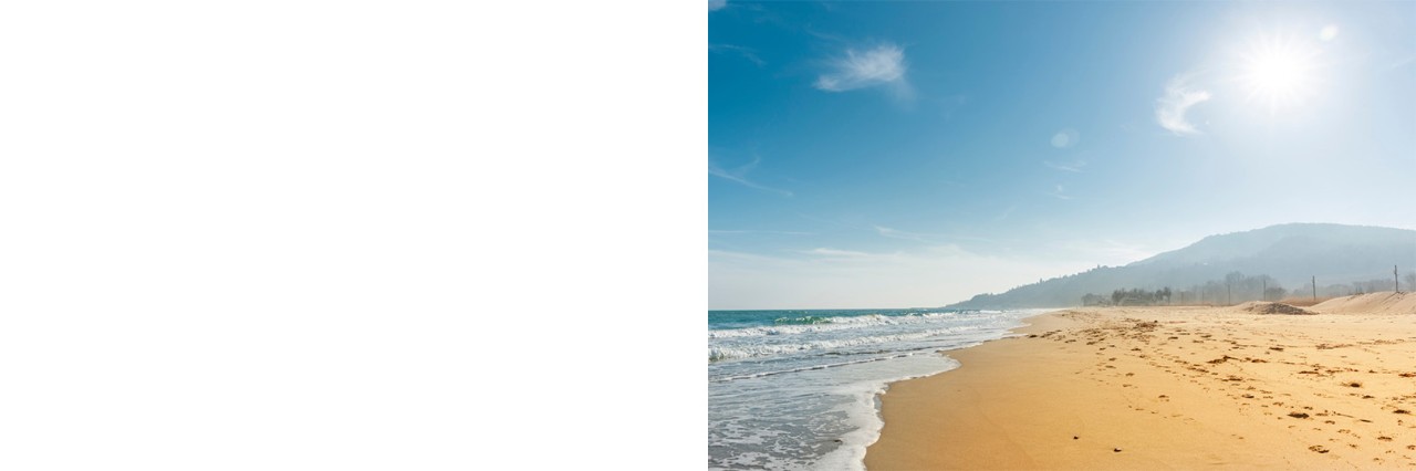 Sandstrand mit ruhigem Meer, dahinter ein sonniger Berg.