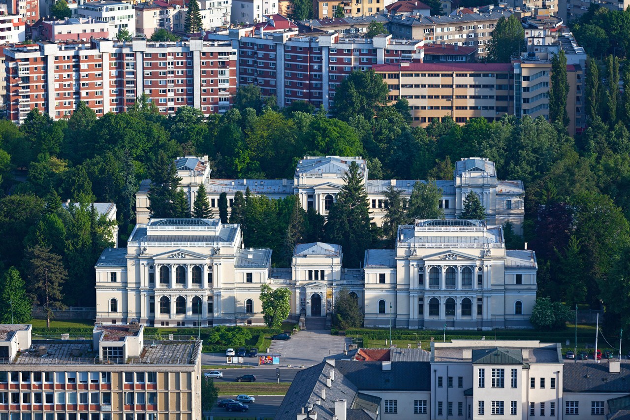 Historischer Museumsbau mit heller Fassade und symmetrischem Innenhof im Stadtgebiet von Sarajevo, umgeben von Wohnhäusern und Grünflächen.
