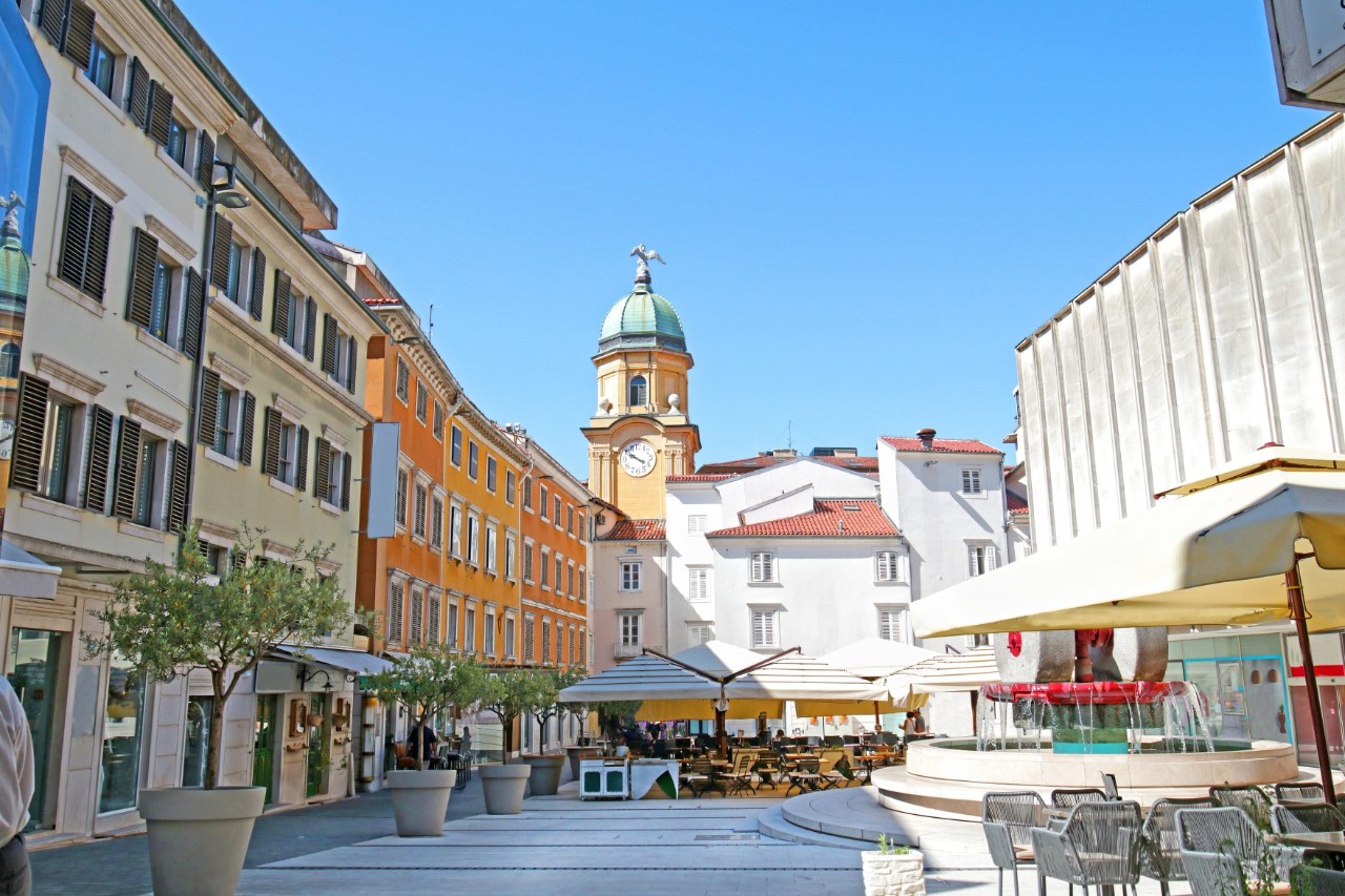 Gelber Stadtturm von Rijeka umgeben von Cafés und Spaziergängern.