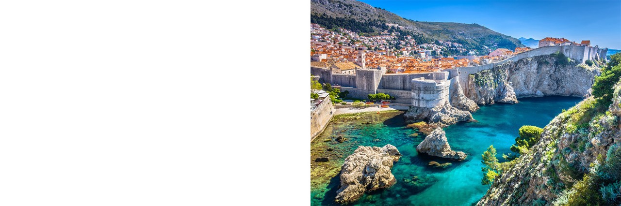 Dubrovnik, die auf eine Steilklippe gebaut und von einer massiven Stadtmauer umgeben ist. Zahlreiche rote Dächer sind zu sehen. Innerhalb der Stadtmauer befinden sich zwei größere Festungsanlagen. Aus dem türkisblauen Meer vor der Stadt ragen mehrere kleine Felsen empor. Auf der rechten Seite ragt eine grün bewachsene Klippe aus dem Bild.