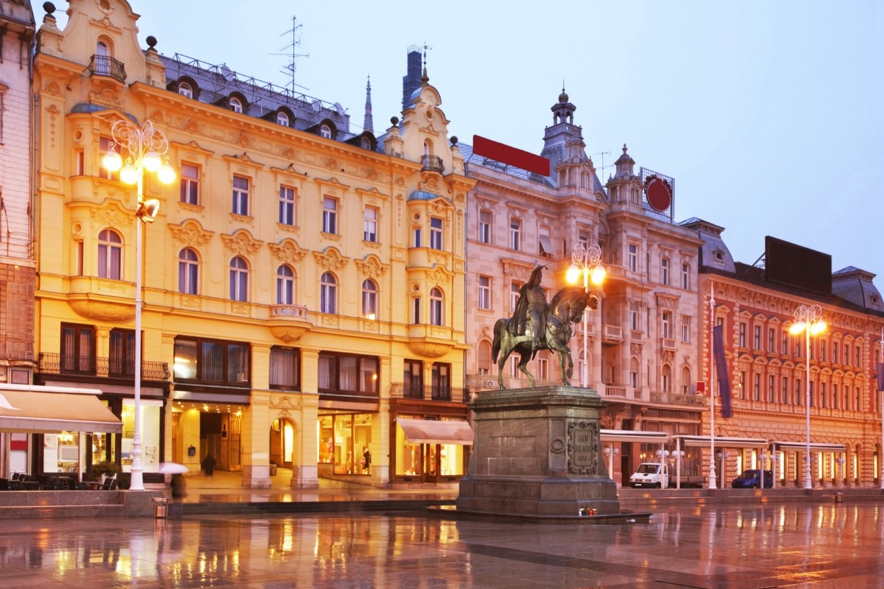 Aneinandergereihte Häuser mit dekorativer Architektur, Reiterstatue im Vordergrund, Abendstimmung 