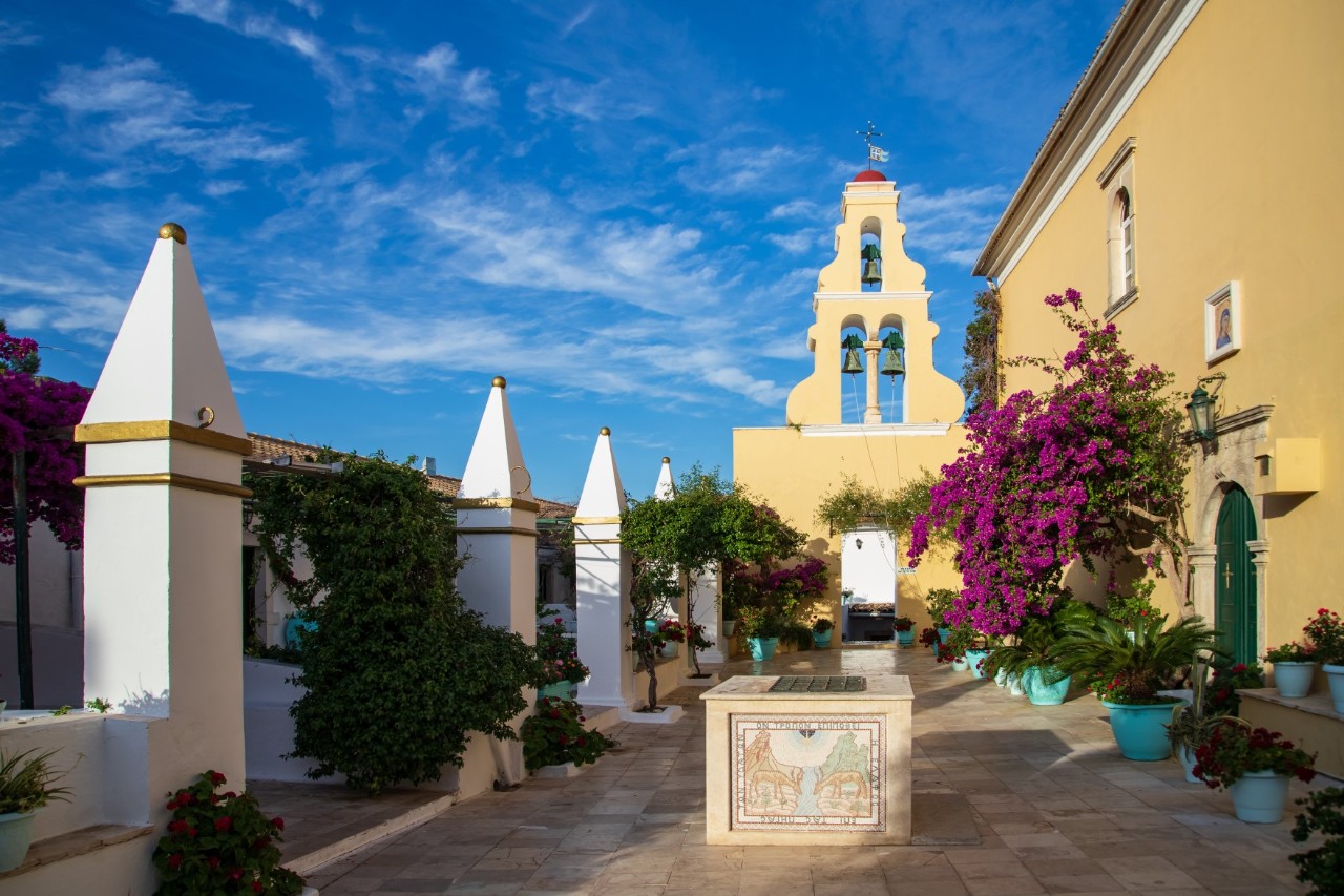 Mediterraner Innenhof mit Glockenturm und bunten Blumen.