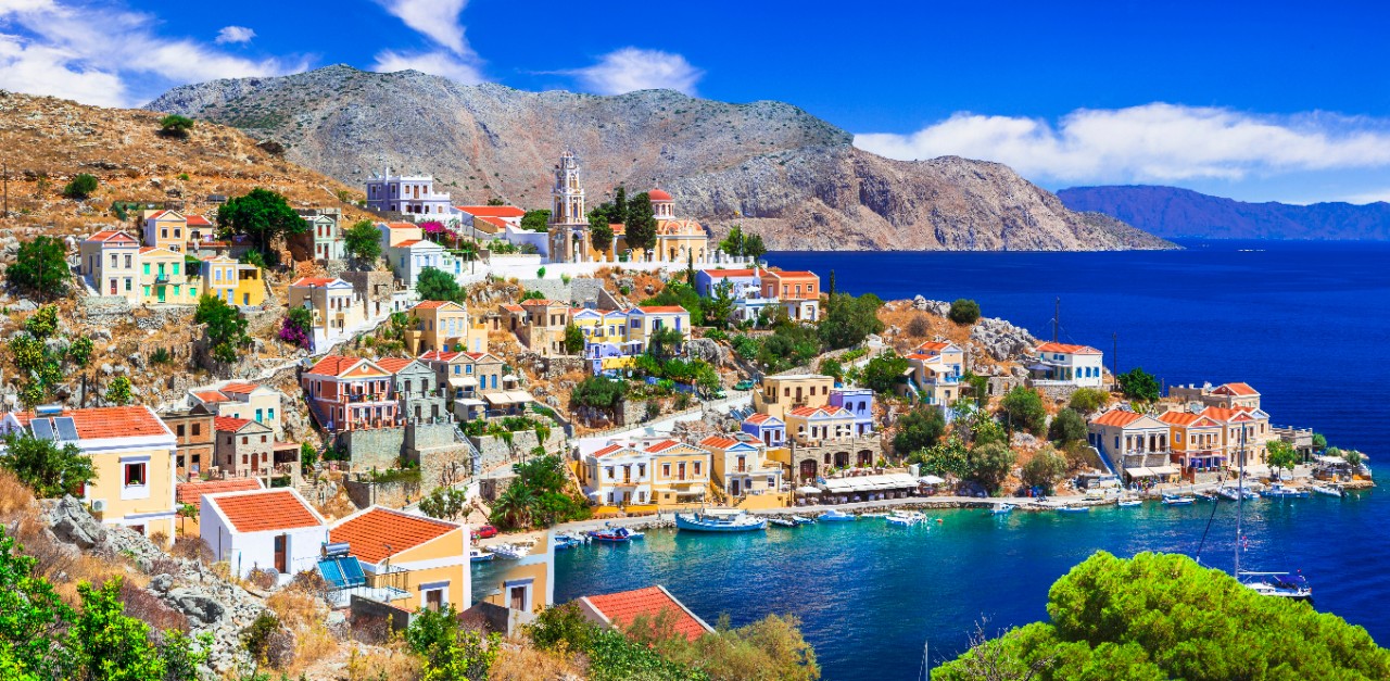 Bunte Häuser am Hafen von Symi mit Booten im klaren Wasser.