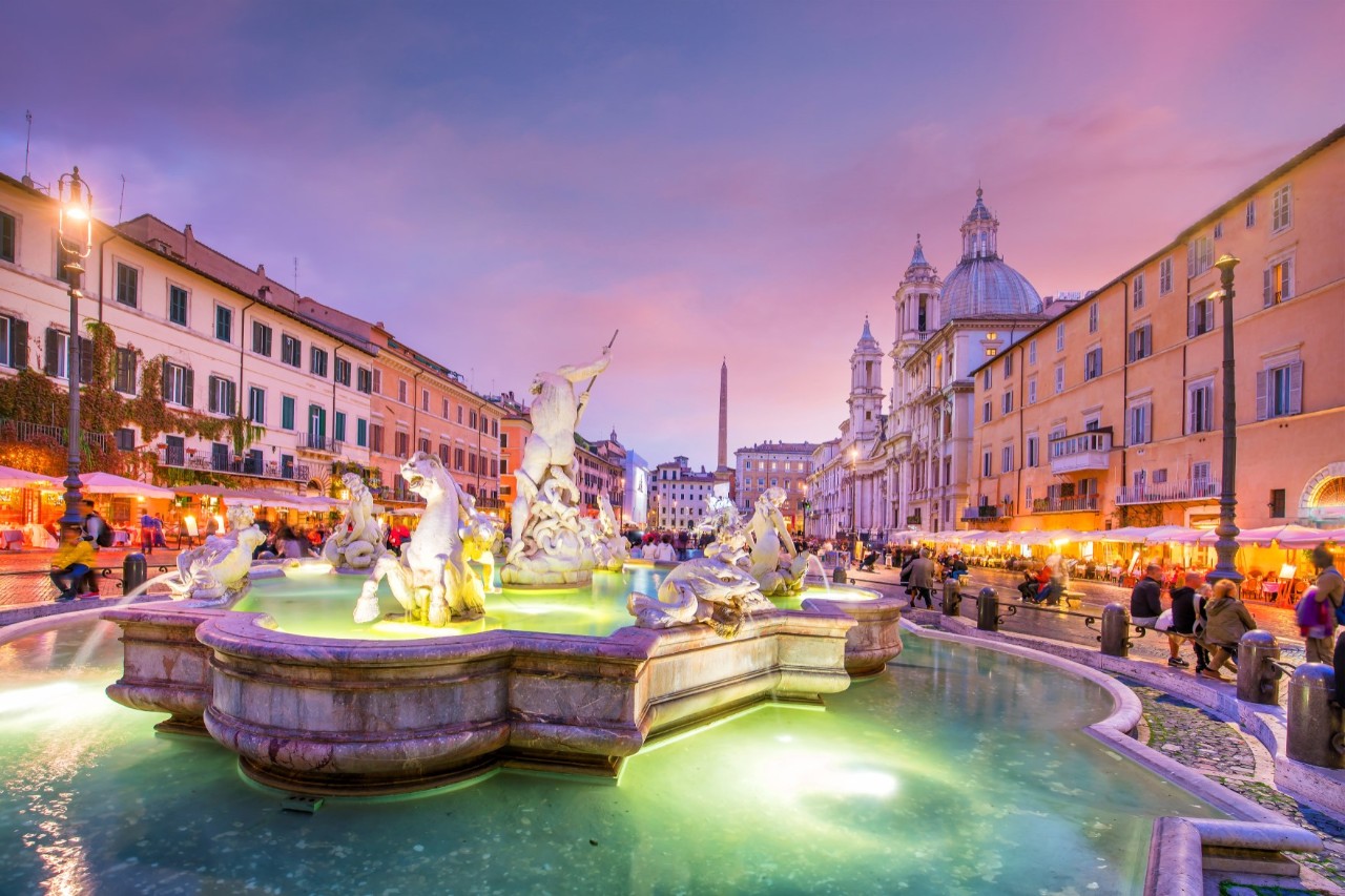 Beleuchteter Brunnen auf der Piazza Navona bei Sonnenuntergang.