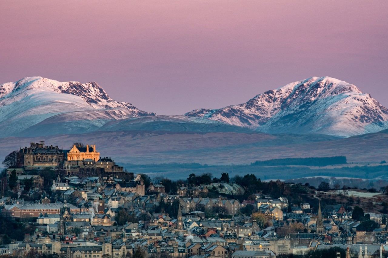 Stirling Castle auf Felsen mit schneebedeckten Bergen im Hintergrund.