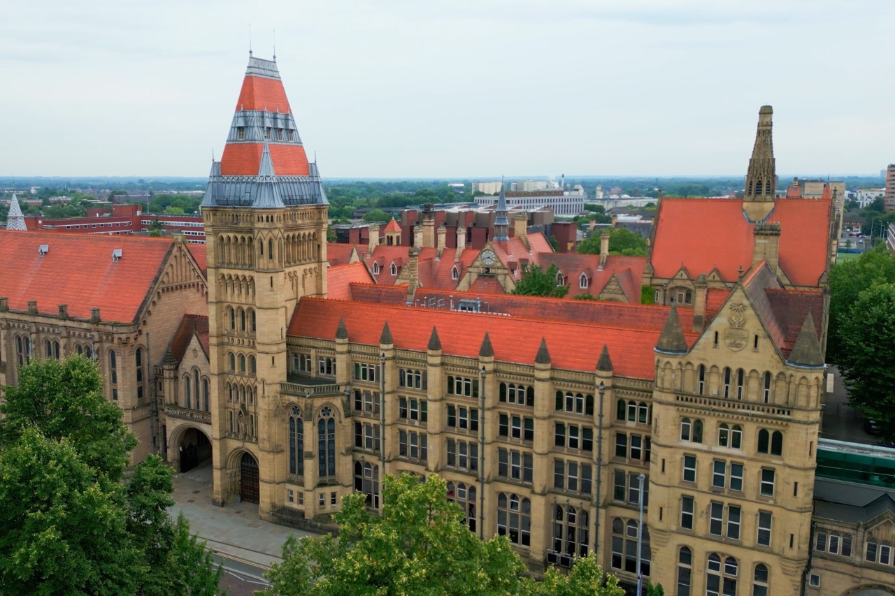 Manchester Museum im neugotischen Stil, ringsherum Bäume und Häuser.