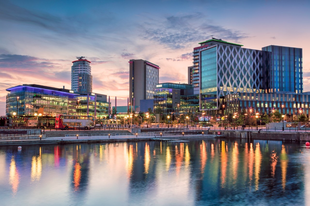 Blick auf Salford Quays, Hochhäuser und beleuchtete Promenade am Kanal.