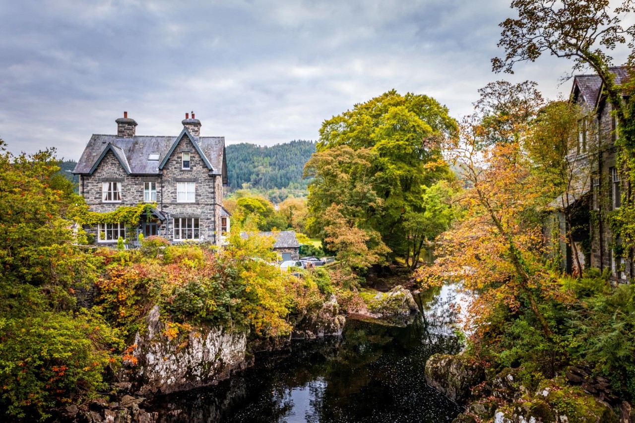 Historisches Haus aus Stein, im Vordergrund kleiner Fluss, grüne Pflanzen, Bäume 