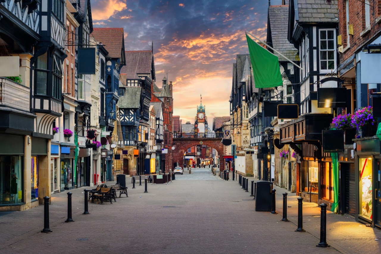 Ruhige Fußgängerzone in der Altstadt von Chester, links und rechts alte Fachwerkhäuser mit Shops, im Hintergrund Kirchturm 