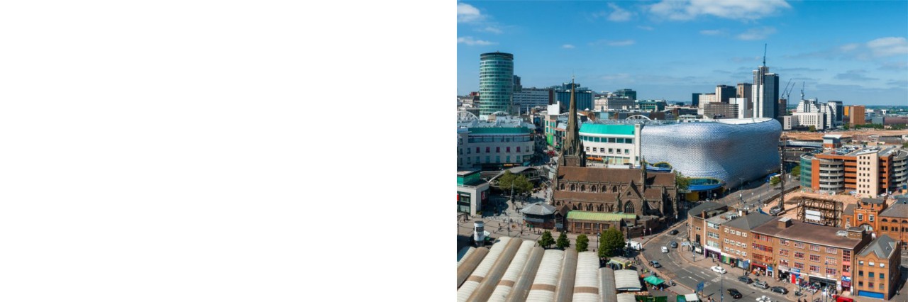 Luftaufnahme von Birmingham: Das Panoramabild zeigt eine dicht bebaute Stadt mit modernen und historischen Gebäuden. Im Vordergrund ist eine belebte Straße und eine Kirche mit spitzem Turm zu sehen. Dahinter ragen Wolkenkratzer und ein großes modernes silberfarbenes, wellenförmiges Haus hervor. Die Szene ist hell erleuchtet und vermittelt ein Gefühl von urbaner Aktivität und Entwicklung. 