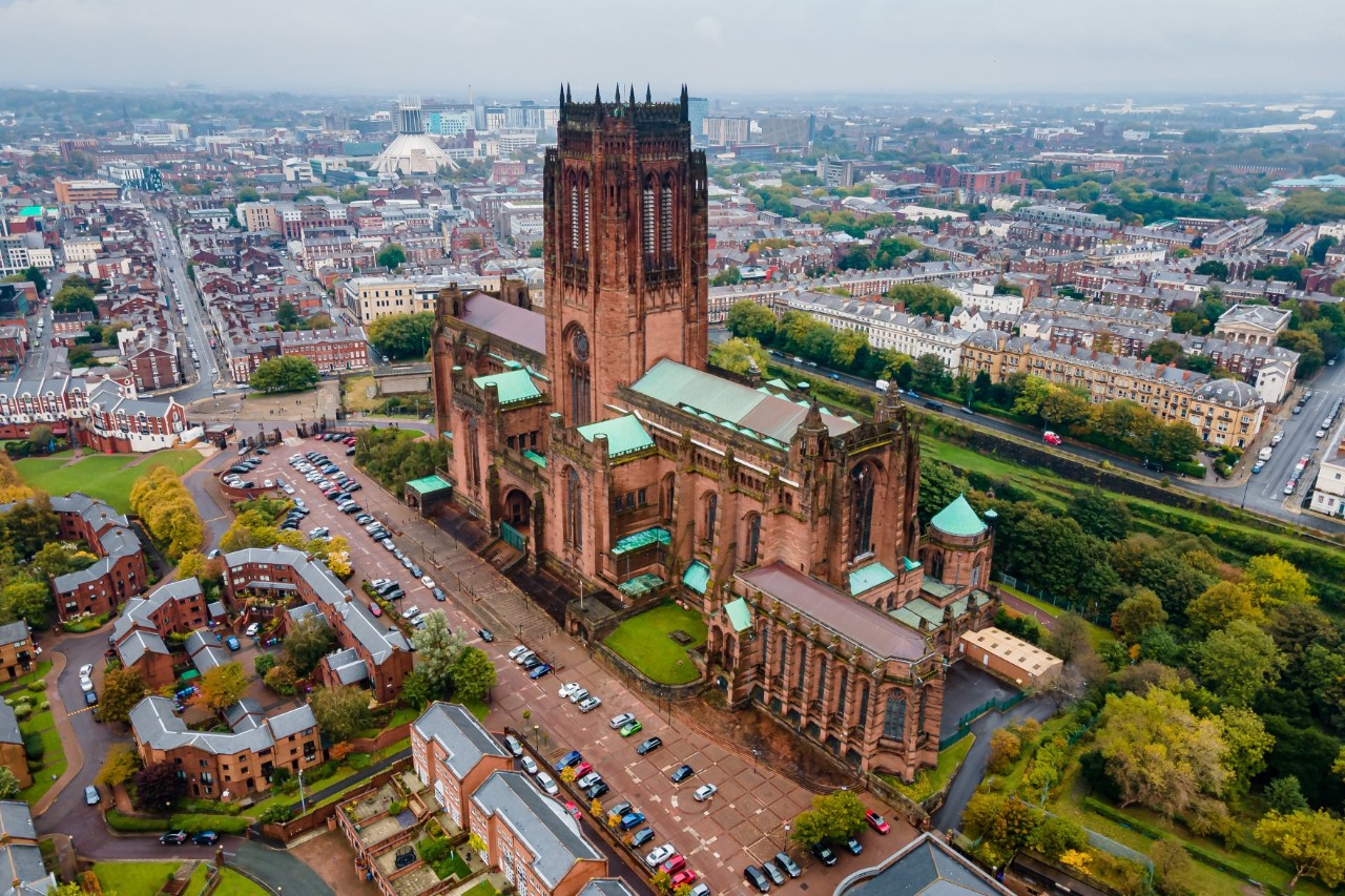 Luftaufnahme einer großen gotischen Kathedrale, die von einem urbanen Umfeld mit Wohnhäusern, Straßen und Parks umgeben ist. 