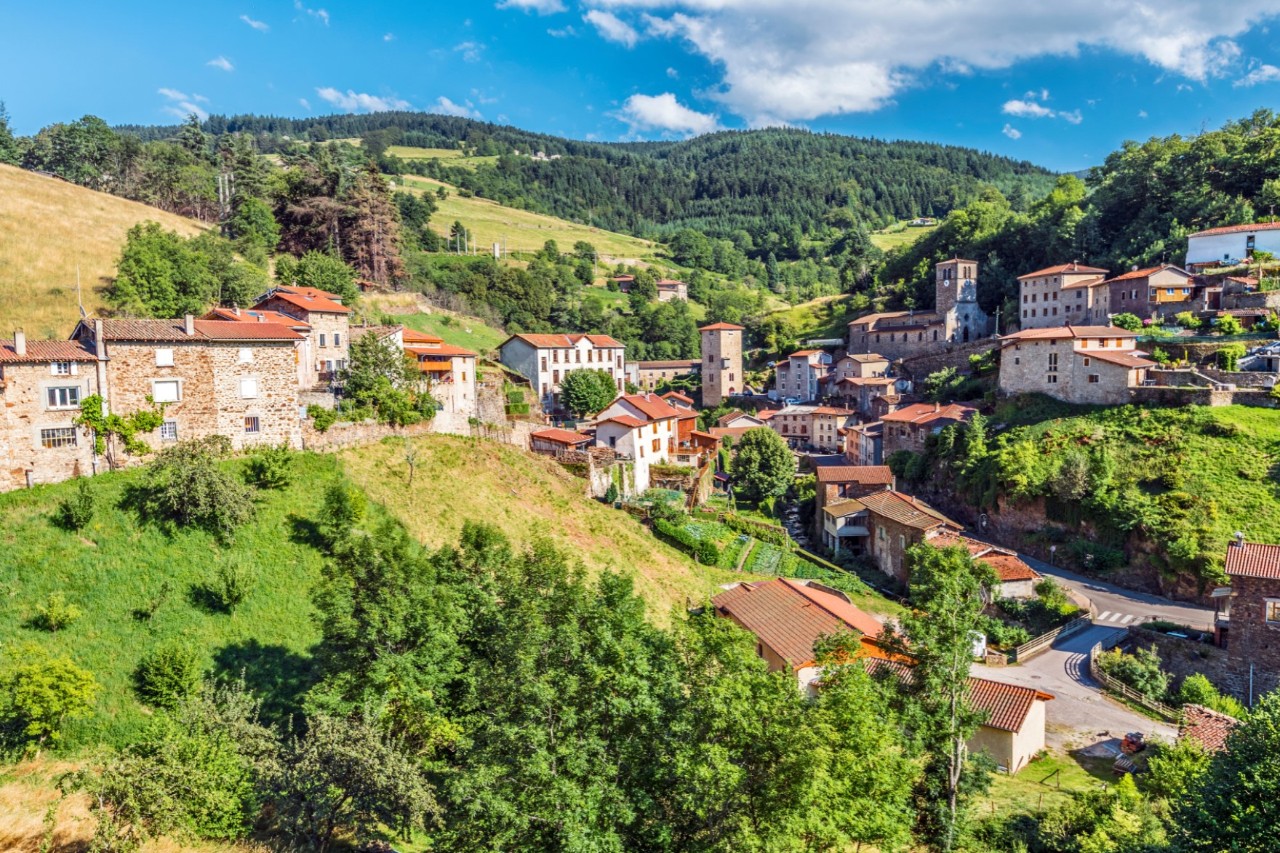 Kleines Dorf mit historischen Häusern umgeben von grünen Hügeln.