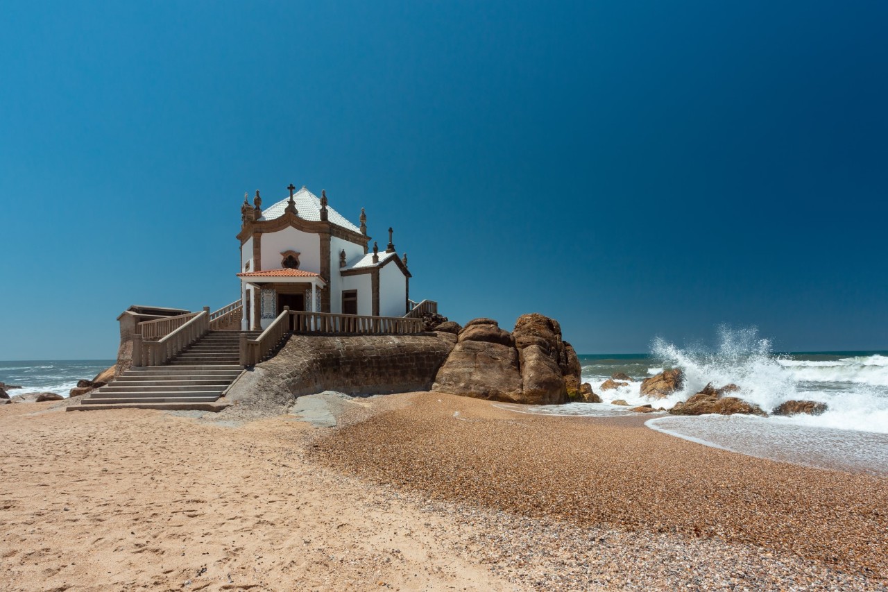 Kapelle Senhor da Pedra auf einem Felsenstrand bei Wellen umgeben.