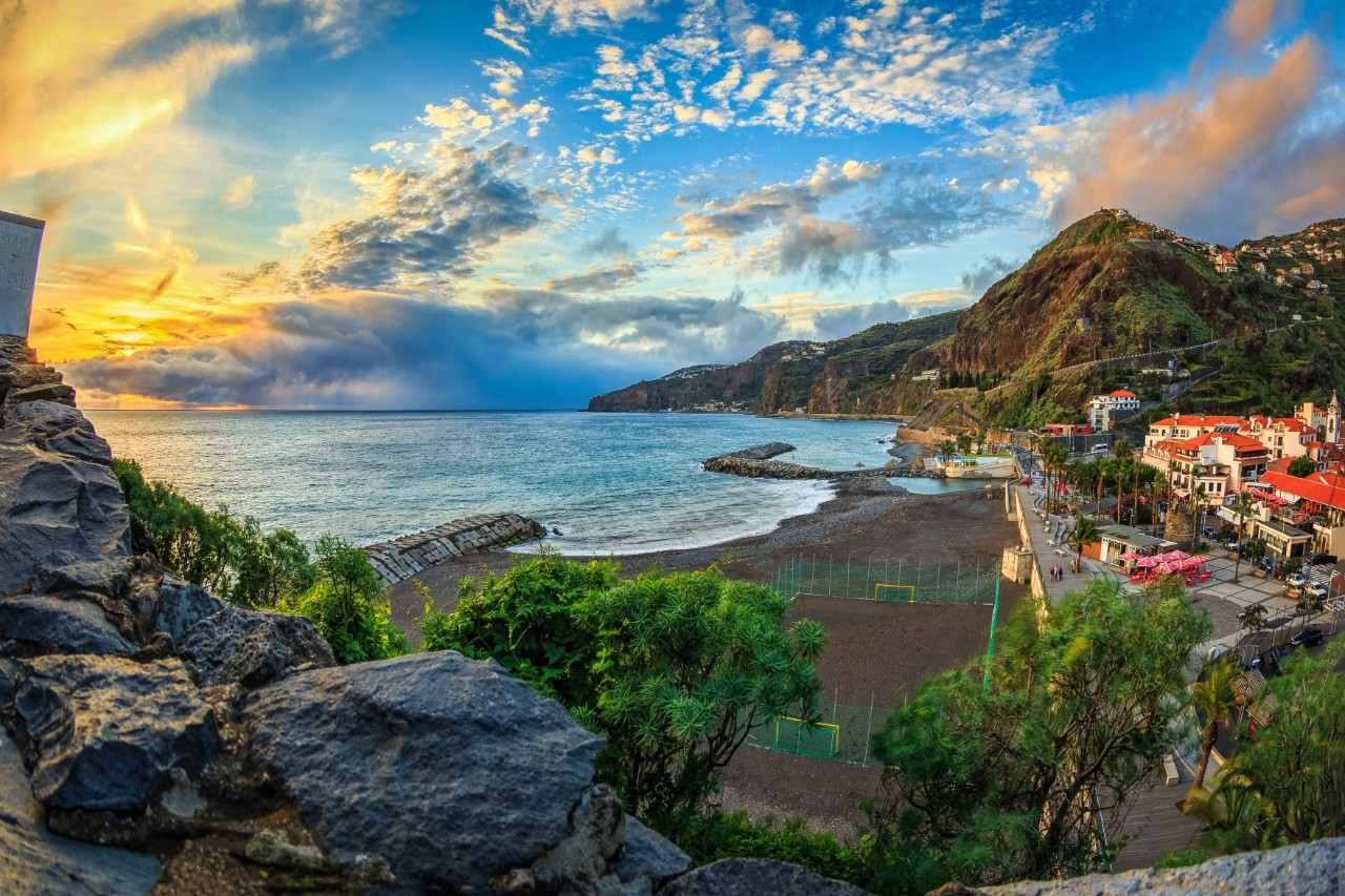 Sonnenuntergang an einem schwarzen Strand vulkanischen Ursprungs, rechts im Bild der Ort Ribeira, im Hintergrund bergige Küste 
